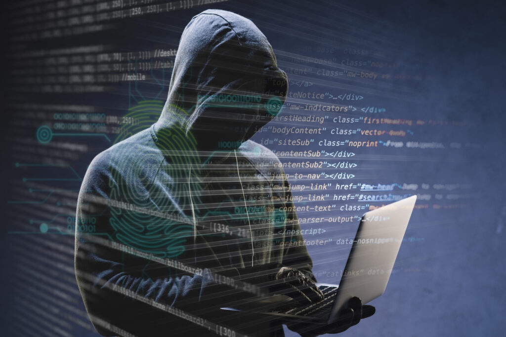 Hacker encapuchonné travaillant sur un ordinateur portable avec des lignes de code superposées en arrière-plan, représentant une cyberattaque ou la cybersécurité.